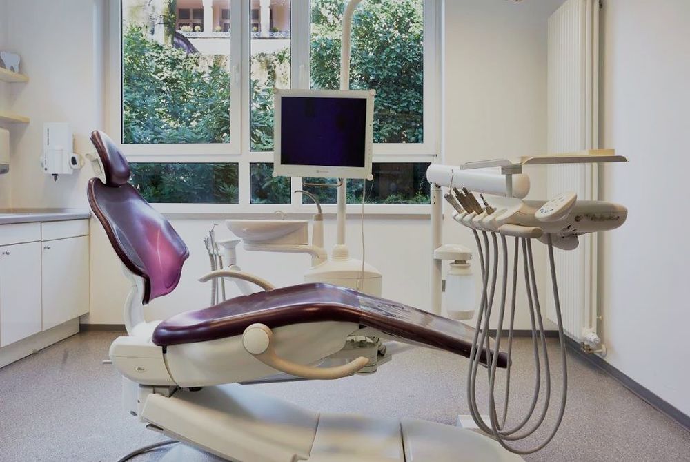 Behandlungszimmer der Praxis mit Behandlungsstuhl, Bildschirm und Fenster ins Grüne